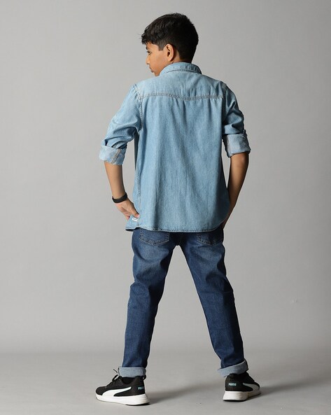 A studio shot of a young man in a black shirt, blue jeans and leather shoes  showing off his watch against a grey background. – Stock Editorial Photo ©  Adamo.Boccittio #255070916