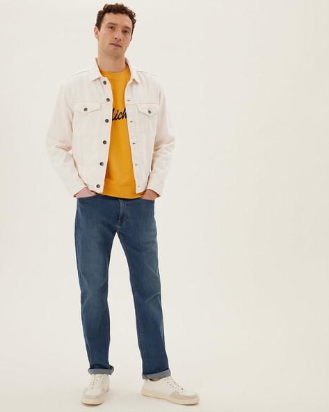 Brunette handsome man in white t-shirt and black pants walks on crosswalk.  Cool guy in denim jacket Stock Photo by look_studio